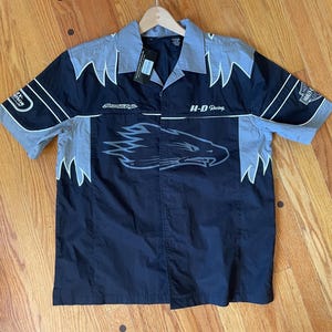 Op de afbeelding: Zwart en grijs overhemd met korte mouwen en een Harley-Davidson Racing-ontwerp. Voorzien van een adelaarsafbeelding op de voorkant en sponsorlogo's op de mouwen. Inclusief een label.