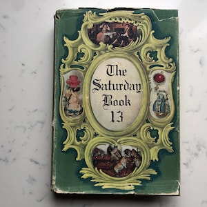 May include: Vintage hardcover book titled "The Saturday Book 13." The cover is green with ornate gold-colored framing around the title and illustrations. The book's cover has a worn appearance, suggesting age and use.