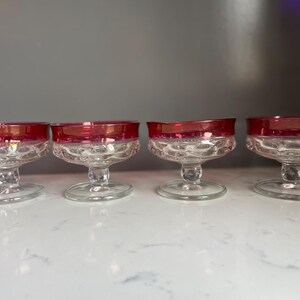 Puede incluir: Cuatro copas de champán vintage con bordes rojo rubí. Los cuencos de vidrio transparente tienen un patrón texturizado y los tallos son cortos y elegantes. Perfectas para servir cócteles o vino espumoso.