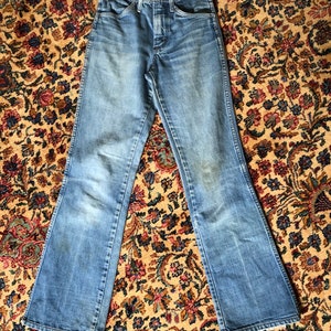 May include: Light blue denim jeans with a flared leg design. The jeans have a button and zipper closure, front and back pockets, and belt loops. The denim has a faded appearance, with some lighter areas. A small tag is attached to the jeans.