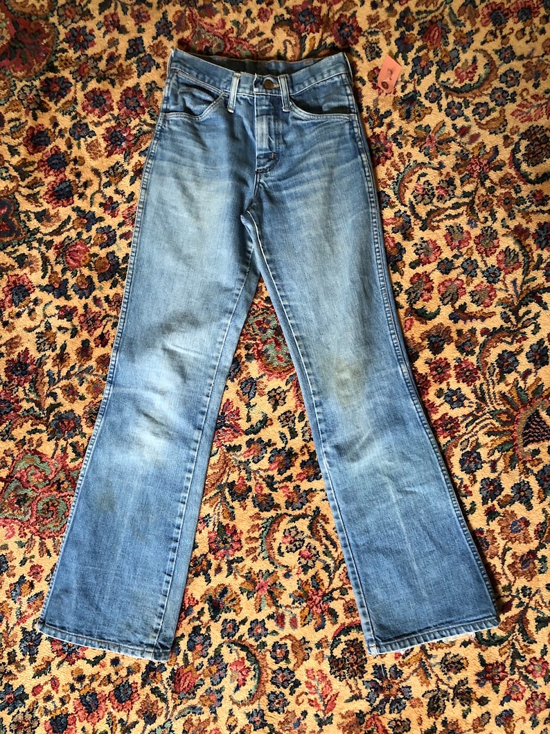 May include: Light blue denim jeans with a flared leg design. The jeans have a button and zipper closure, front and back pockets, and belt loops. The denim has a faded appearance, with some lighter areas. A small tag is attached to the jeans.