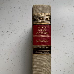 May include: A vintage book titled "Essays Poems Addresses" by Emerson. The book has a tan linen cover with gold accents and a red spine. The spine features the title, author, and "Classics Club" in gold lettering.