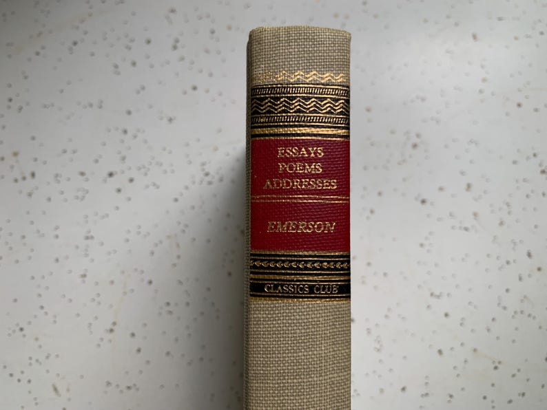 May include: A vintage book titled "Essays Poems Addresses" by Emerson. The book has a tan linen cover with gold accents and a red spine. The spine features the title, author, and "Classics Club" in gold lettering.