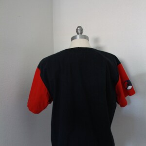 May include: Black t-shirt with red sleeves. The sleeves have a small design on the left sleeve. The shirt is displayed on a mannequin. The shirt is a casual style.