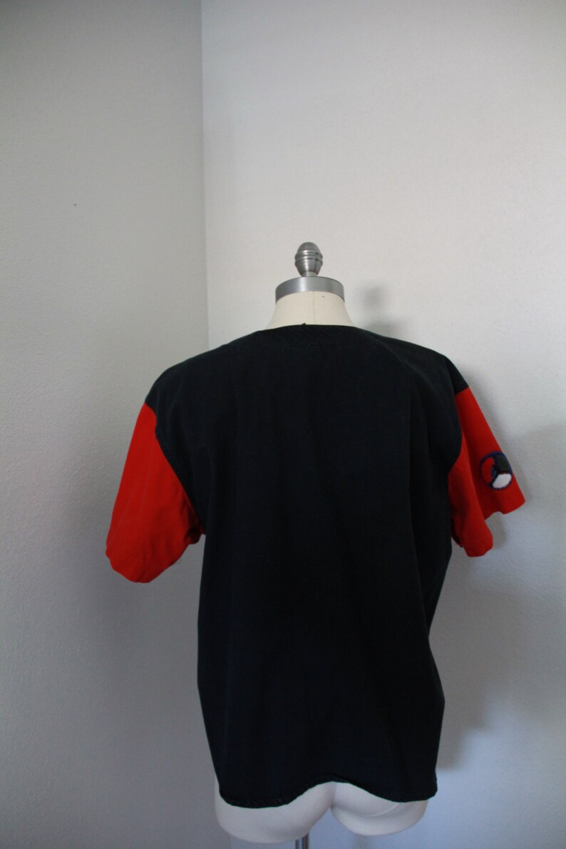 May include: Black t-shirt with red sleeves. The sleeves have a small design on the left sleeve. The shirt is displayed on a mannequin. The shirt is a casual style.