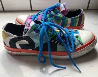 Könnte beinhalten: Ein Paar bunte Leinenschuhe mit blauen Schnürsenkeln. Die Schuhe weisen eine Mischung aus Mustern auf, darunter Streifen und abstrakte Formen, mit einer weißen Zehenkappe und orangefarbenen Zierleisten. Das Wort "Jams" ist auf der Seite sichtbar.