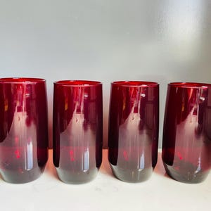 Könnte beinhalten: Vier stiellose Weingläser in tiefroter Farbe. Die Gläser haben einen abgerundeten Boden und eine leicht konische Form, ideal zum Servieren von Wein oder anderen Getränken. Die Gläser bestehen aus einem transparenten Material, wodurch die Farbe des Getränks sichtbar wird.