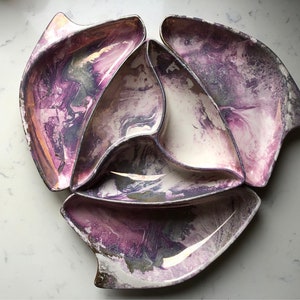 Puede incluir: Un conjunto de cinco fuentes decorativas. Cada fuente tiene una forma única con un borde plateado y un diseño veteado en morado y blanco. Las fuentes están dispuestas en un patrón circular, ideal para servir aperitivos o snacks.