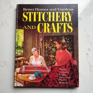 May include: A vintage book cover for "Better Homes and Gardens Stitchery and Crafts" featuring two women working on crafts. The cover has yellow text and a photo of women crafting. The book lists various crafts like weaving and knitting.