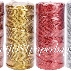 May include: Four spools of metallic thread, each in a different colour: rose gold, gold, red, and silver. The spools are wrapped in clear plastic.