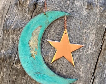 Puede incluir: Una luna creciente azul turquesa con detalles dorados cuelga de un alambre de cobre con un colgante de estrella de cobre.