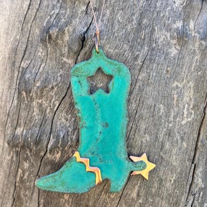 May include: A turquoise blue metal cowboy boot ornament with a star cut out and a copper spur. The ornament has a copper wire hanger.