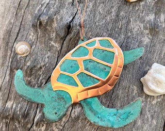 May include: A teal green and copper turtle ornament with a detailed shell design. The ornament is hanging from a copper string.