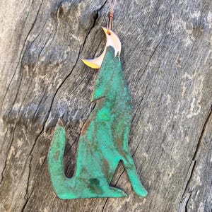 May include: A green metal wolf silhouette with a copper crescent moon on top. The wolf is howling at the moon. The metal has a rustic, aged look.