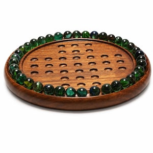 May include: A circular wooden solitaire board game featuring a natural brown wood grain finish with a series of indented holes arranged in a cross pattern. The perimeter of the board is lined with numerous translucent green glass marbles.