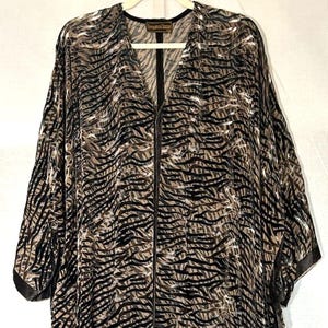 May include: A flowing, open-front kimono-style top with a zebra stripe pattern in shades of brown, black, and tan. The top features a V-neckline, a full-length zip, and wide sleeves. The bottom hem and sleeve edges are trimmed with a dark brown border.