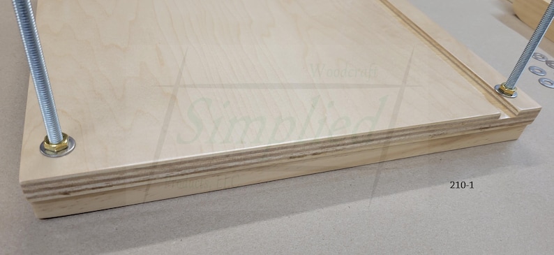 May include: A light-colored wooden board with a visible layered plywood edge, featuring two vertical threaded metal rods secured with nuts and washers at the corners. The surface displays a faint logo and the text 210-1 printed on the side.