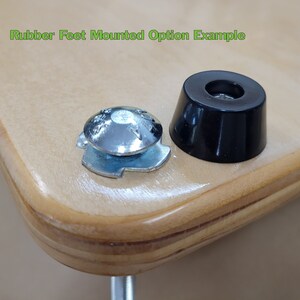 May include: Close-up of two rubber feet, one mounted on a piece of wood. The rubber feet are black and have a small hole in the center. The text "Rubber Feet Mounted Option Example" is visible in the top left corner of the image.