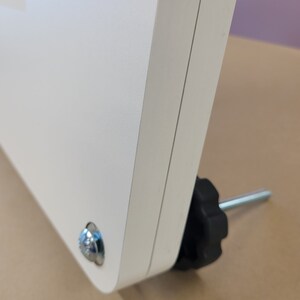 May include: White metal stand with a black knob and a silver screw. The stand has a textured surface.