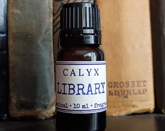 May include: A small amber glass bottle with a black screw-top cap and a white label. The label features the text CALYX LIBRARY and botanical 10 ml fragrance in blue ink. The bottle is cylindrical with a narrow neck and a flat base for stability.