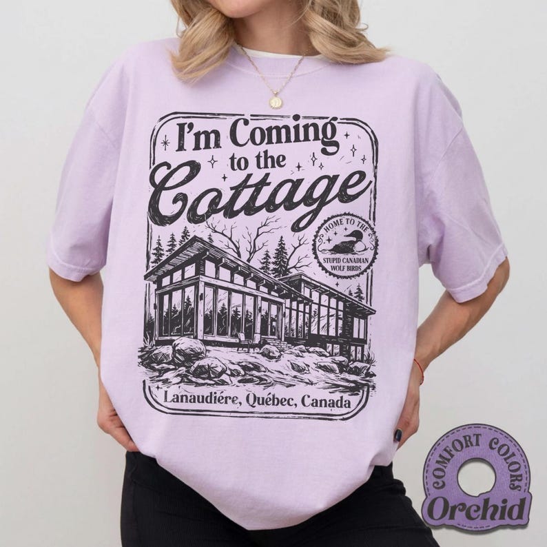 Puede incluir: Camiseta lila claro con un dise&ntilde;o negro que dice "I'm Coming to the Cottage" sobre una ilustraci&oacute;n de una caba&ntilde;a moderna. El texto "Lanaudi&egrave;re, Qu&eacute;bec, Canada" est&aacute; debajo. La camiseta es de color Orchid.