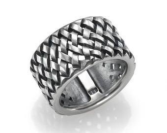 May include: A silver-colored ring with a woven design. The ring has a wide band with a textured, basket-weave pattern. The inside of the ring is smooth and has the number "925" stamped on it. The ring is displayed on a white background.