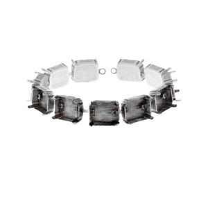 Puede incluir: Un brazalete plateado compuesto por engastes cuadrados, con la parte trasera abierta, unidos en un arreglo circular. Cada engaste tiene cuatro garras que se extienden desde las esquinas, diseñadas para sujetar una piedra preciosa u otro elemento decorativo. El brazalete se muestra sobre un fondo blanco.