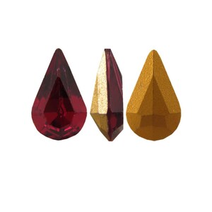 May include: Three faceted teardrop-shaped gemstones. One is a deep red, another has a gold and red combination, and the third is solid gold. The gems are displayed against a white background, showcasing their cut and color.