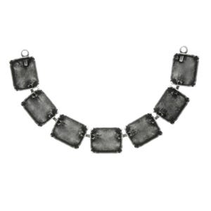 Puede incluir: Un collar plateado con siete piedras rectangulares de color gris oscuro. Cada piedra está conectada por pequeños eslabones plateados, formando una forma curva. El collar tiene un lazo en cada extremo para sujetarlo.