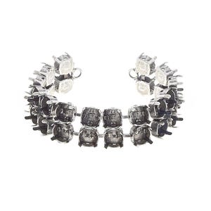 May include: A silver-toned metal bracelet base featuring two parallel rows of empty, pronged settings designed to hold square-shaped stones. The bracelet has a flexible, open-ended design with small circular loops at each end for fastening.