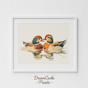 May include: Watercolour print of two mandarin ducks on water. The ducks have orange, brown, green, and white feathers. The print is in a white frame and is against a white wall. The print is from DreamCache Prints.