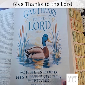 May include: An open Bible page featuring the text Give Thanks to the Lord and For He is Good; His Love Endures Forever. A colorful illustration of a mallard duck swimming in water surrounded by cattails is centered on the page.