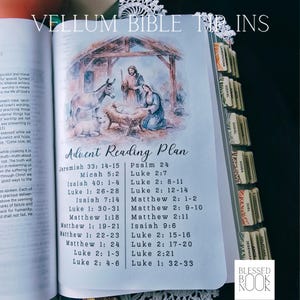 May include: A vellum Bible tip-in page featuring a watercolor illustration of the Nativity scene with a manger, donkey, and sheep. Below the image is the text Advent Reading Plan followed by a list of scripture references. The page has index tabs.