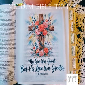 May include: A translucent vellum bible tip-in sheet featuring a wooden cross adorned with pink and orange roses and blue foliage. The text reads, My Sin Was Great, But His Love Was Greater - JOHN 3:16. The page includes decorative book tabs.