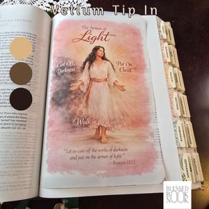 May include: A vellum tip-in page inserted into a book, featuring a watercolor-style illustration of a person in a white robe. Text reads: The Armor of Light, Cast Off Darkness, Put On Christ, Walk in the Light, and Romans 13:12. Book tabs are visible.