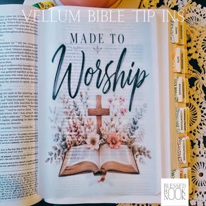May include: A translucent vellum bible tip-in insert featuring the text Made to Worship in dark green script above an illustration of a wooden cross surrounded by pink and white flowers and an open book, with labeled book tabs on the side.