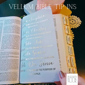 May include: A translucent vellum bible tip-in sheet featuring gold foil calligraphy text. The text lists the five solas: Sola Scriptura, Solus Christus, Sola Fide, Sola Gratia, and Soli Deo Gloria, with English definitions printed below each Latin phrase.