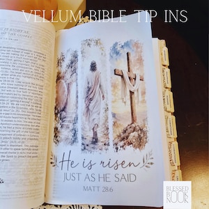 May include: A vellum Bible tip-in page featuring a watercolor illustration of a figure walking toward a cross and an open tomb. The text reads "He is risen JUST AS HE SAID MATT 28:6" and "VELLUM BIBLE TIP INS". The page includes several labeled book tabs.