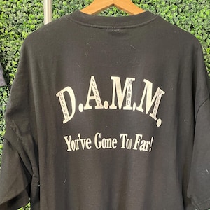 May include: Black t-shirt with white text. The text reads "D.A.M.M. Drivers Against Madd Mothers" above "You've Gone To Far!" in a bold, sans-serif font. The shirt is hanging on a wooden hanger.