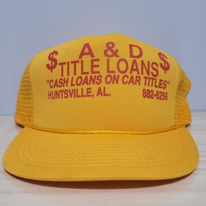 May include: A yellow trucker hat with red text reading "A & D TITLE LOANS". The hat also features the text "CASH LOANS ON CAR TITLES" and the city "HUNTSVILLE, AL."