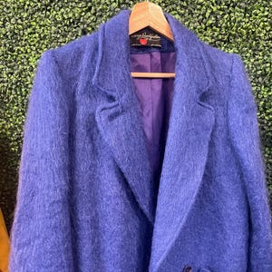 Könnte beinhalten: Ein zweireihiger Blazer in einer leuchtend violetten, flauschigen Textur mit langen Ärmeln, fallendem Revers und zwei Vordertaschen. Das Innere ist mit einem glatten violetten Stoff gefüttert und hat ein Etikett mit Serge Daus Fashion und einem roten Herz.