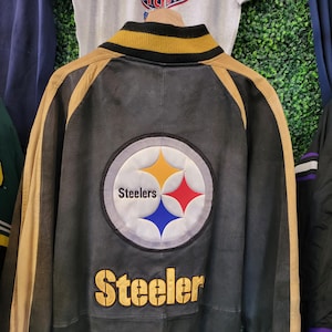 May include: Black and gold leather jacket with the Pittsburgh Steelers logo on the back. The jacket has gold accents on the sleeves and collar, and the word "Steeler" is embroidered in gold.