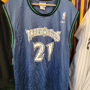 May include: A blue mesh basketball jersey with the words "TIMBERWOLVES" in white script and the number "21" in white. The jersey has black and green trim and the NBA and Reebok logos.