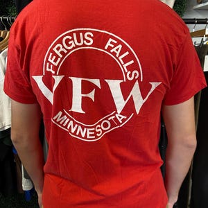Puede incluir: Camiseta roja con un gr&aacute;fico circular blanco en la espalda. El gr&aacute;fico dice "FERGUS FALLS" en la parte superior, "YFW" en el centro y "MINNESOTA" en la parte inferior. La camiseta es de manga corta.
