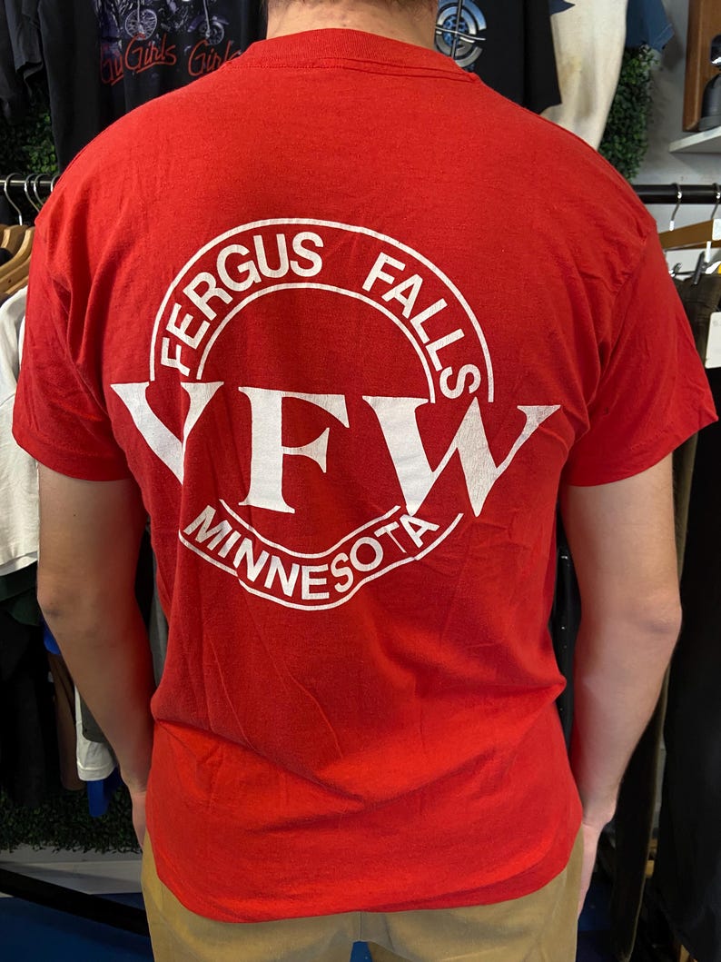 Puede incluir: Camiseta roja con un gr&aacute;fico circular blanco en la espalda. El gr&aacute;fico dice "FERGUS FALLS" en la parte superior, "YFW" en el centro y "MINNESOTA" en la parte inferior. La camiseta es de manga corta.