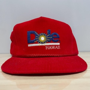 May include: Red corduroy cap with the Dole logo embroidered in blue, yellow, and white. The word "HAWAII" is embroidered below the logo. The cap has a curved brim and a rope detail.