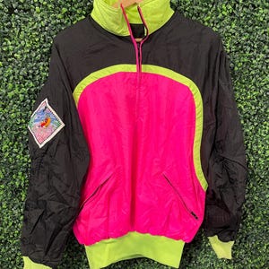 May include: A vintage black, pink, and neon green windbreaker jacket. The jacket features a high collar, a half-zip closure, and a patch on the left sleeve. The design includes a large pink panel on the front and a neon green trim.