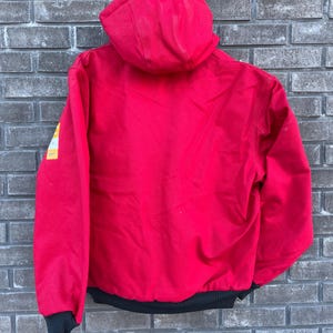Pode incluir: Casaco vermelho com capuz e bainha e punhos canelados pretos. O casaco tem um patch amarelo e branco na manga esquerda. Feito de um material dur&aacute;vel, ideal para atividades ao ar livre.
