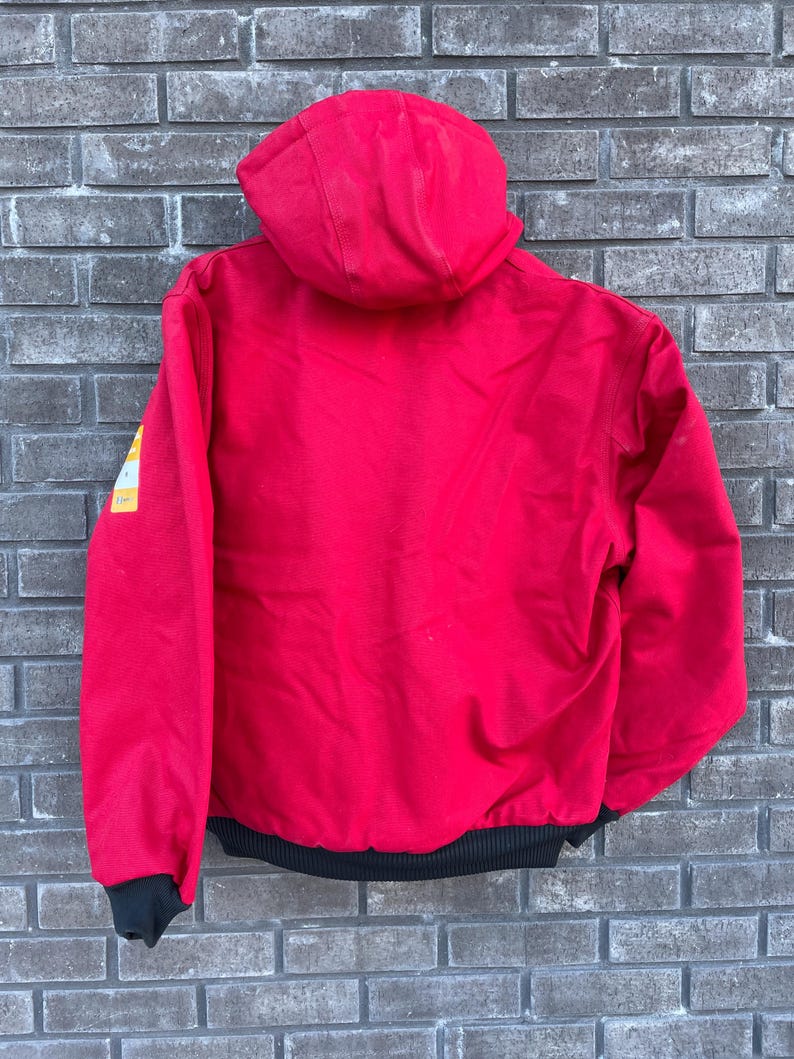Pode incluir: Casaco vermelho com capuz e bainha e punhos canelados pretos. O casaco tem um patch amarelo e branco na manga esquerda. Feito de um material dur&aacute;vel, ideal para atividades ao ar livre.