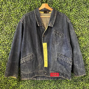 May include: A dark blue denim jacket featuring a lime green vertical panel along the button placket, a red rectangular patch with black text at the bottom, and a black and white houndstooth patterned lining inside the collar area.
